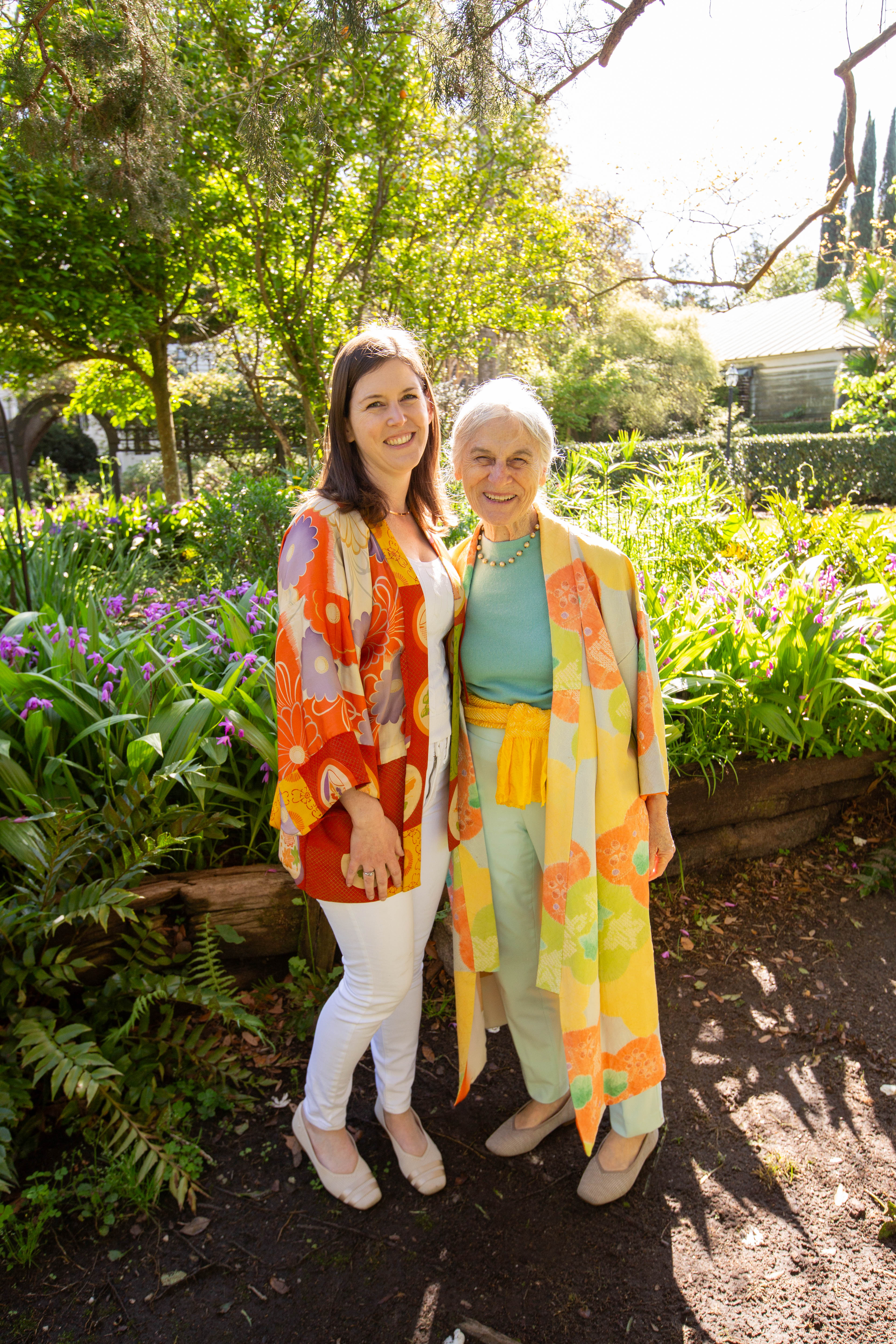 Two women standing in a garden wearing colorful scarves.