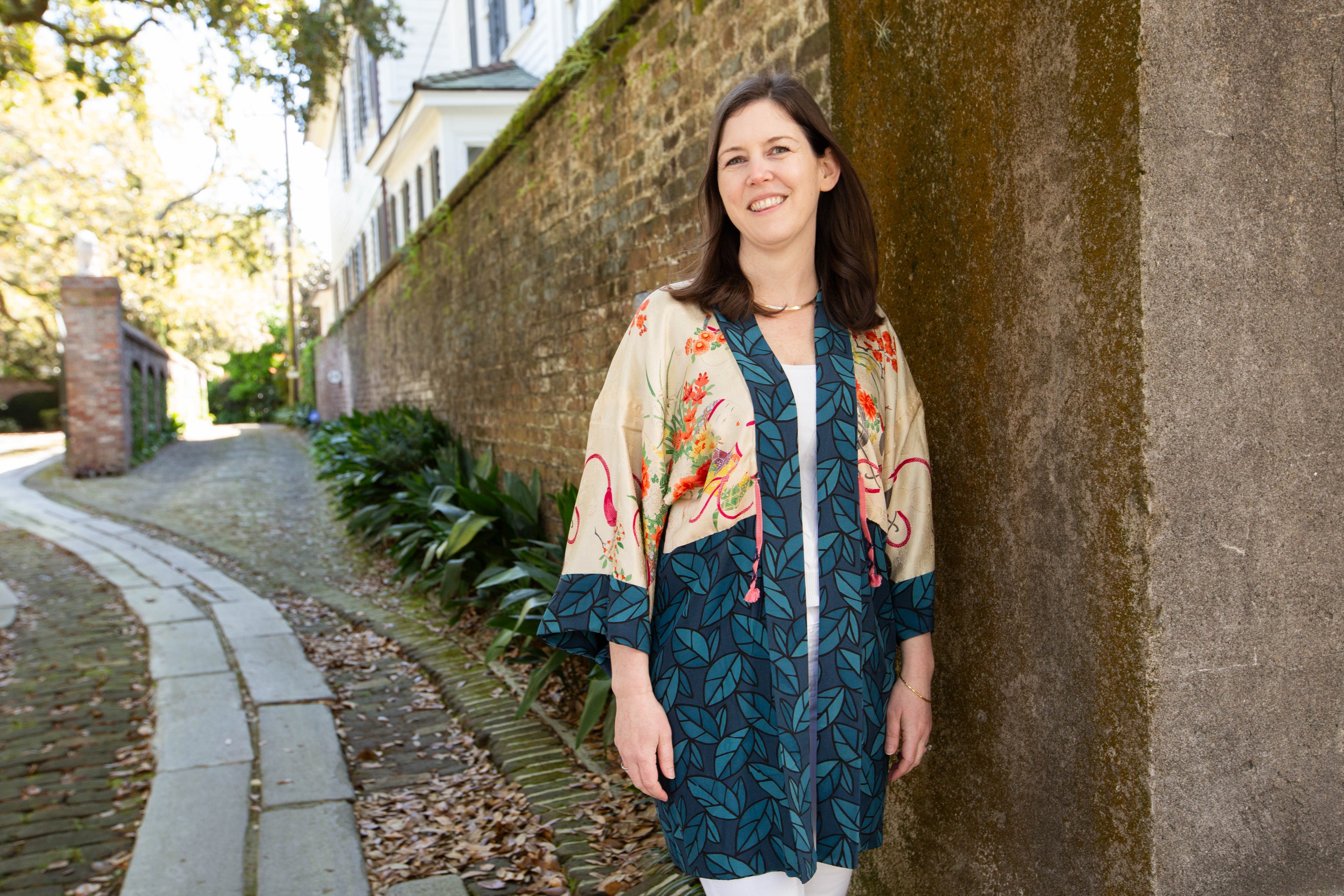 Nancy, Owner of Kiku wearing a floral kimono-style jacket standing against a stone wall.