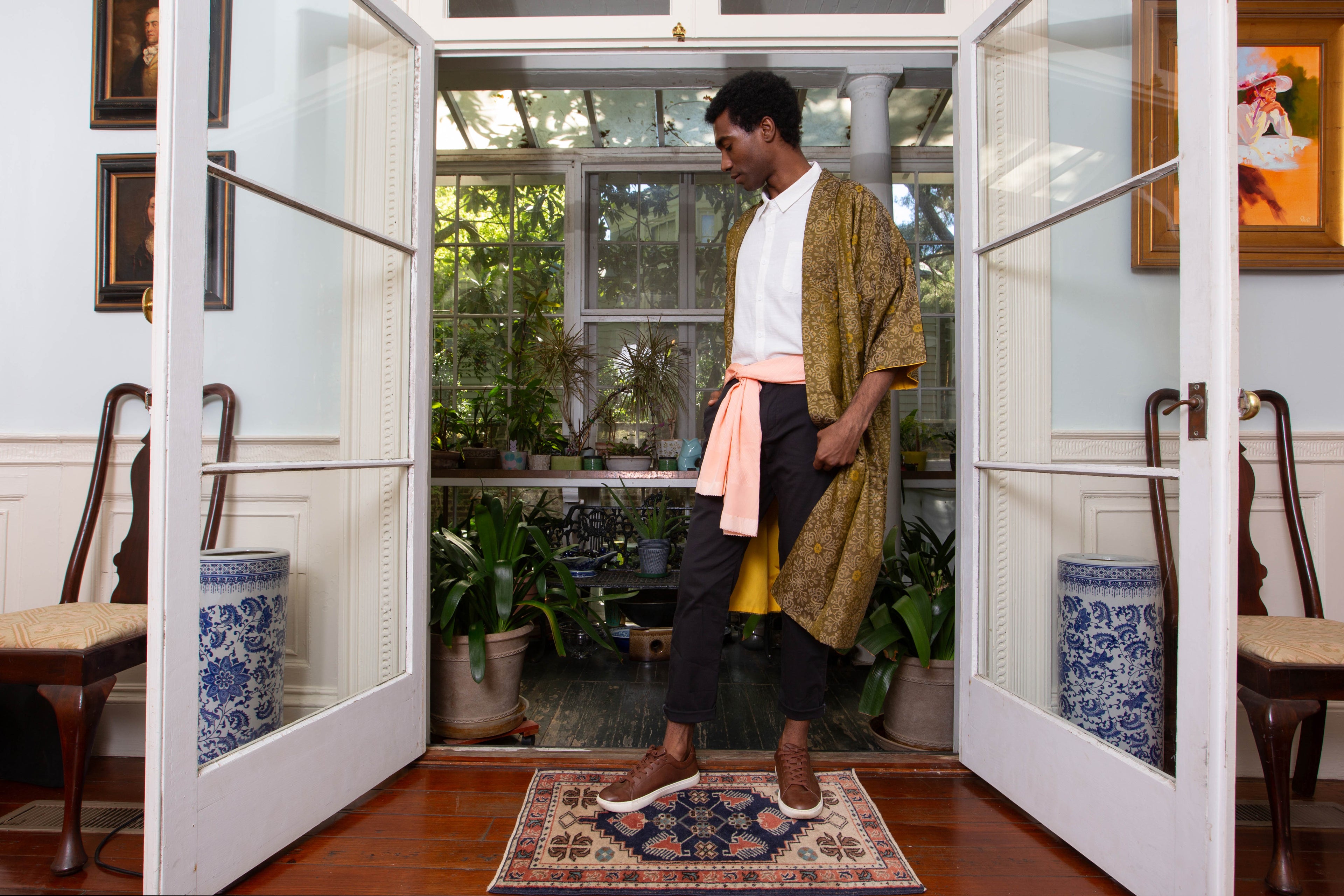 Person standing in a room with open doors, leading to a garden with plants and furniture.
