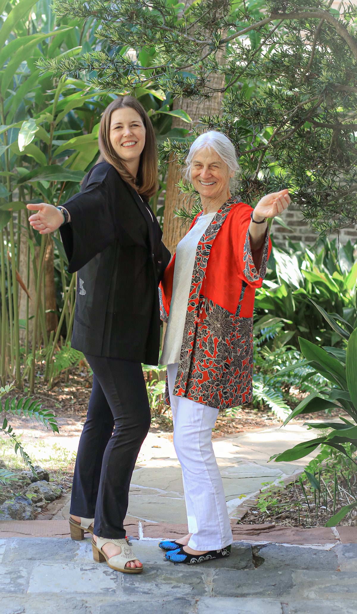 Two women standing outdoors with greenery in the background